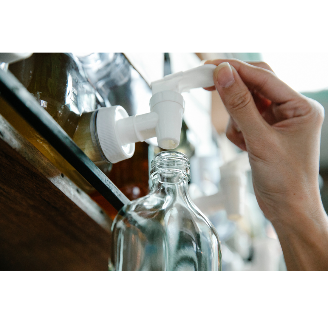glass bottle being filled from a jug with a white spout on a wooden shelf 