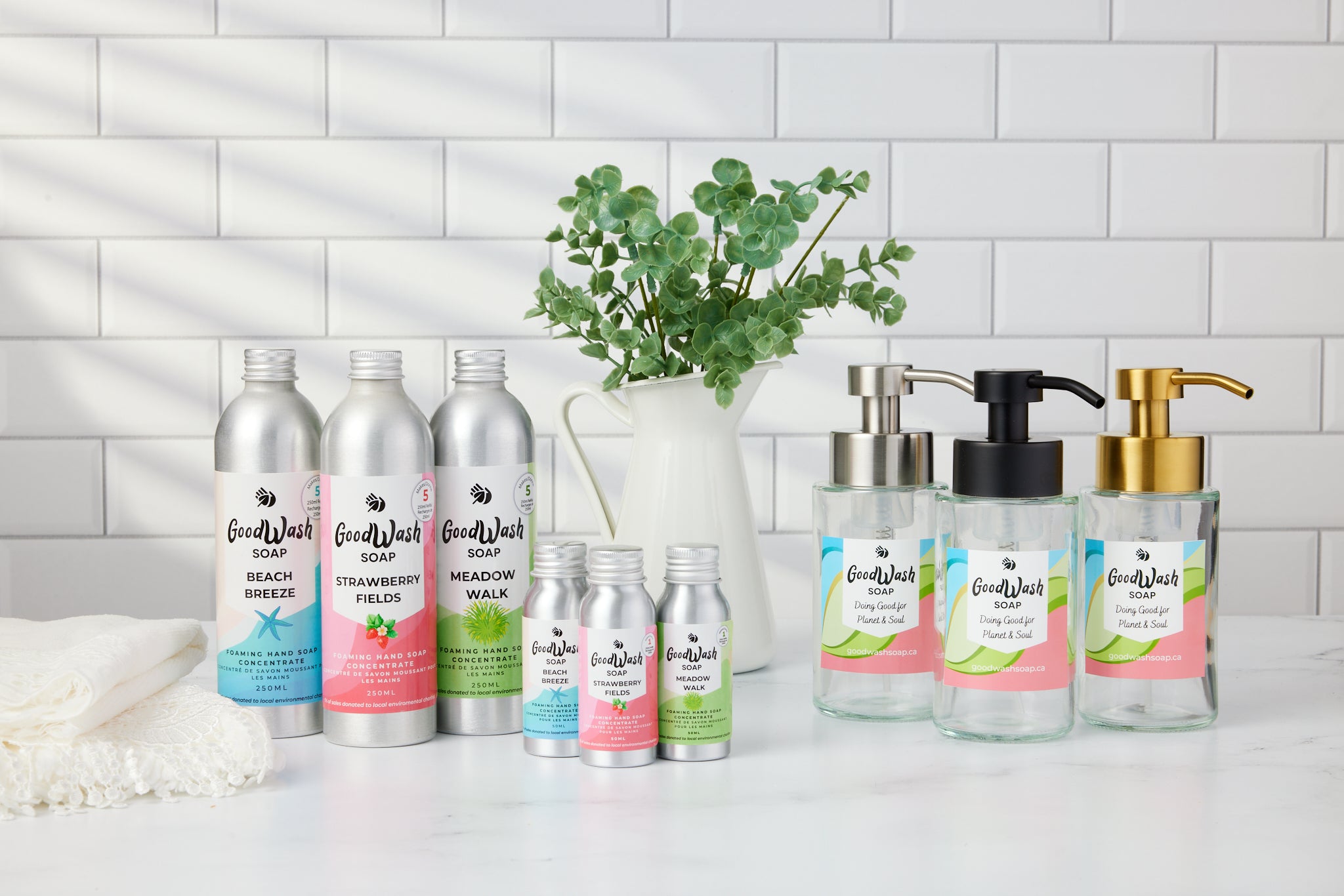 A bathroom counter with bottles of foaming hand soap concentrate in aluminum bottles with colorful lables and glass foaming hand soap dispensers